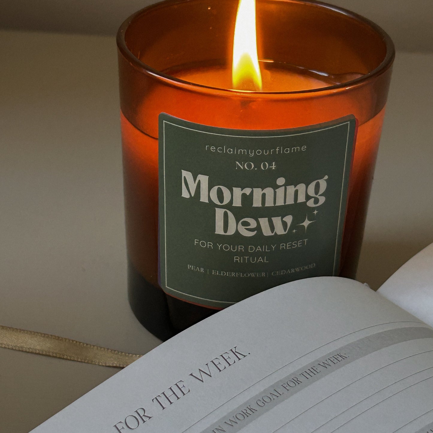 Candle labeled 'Morning Dew' on an open notebook with a pen.