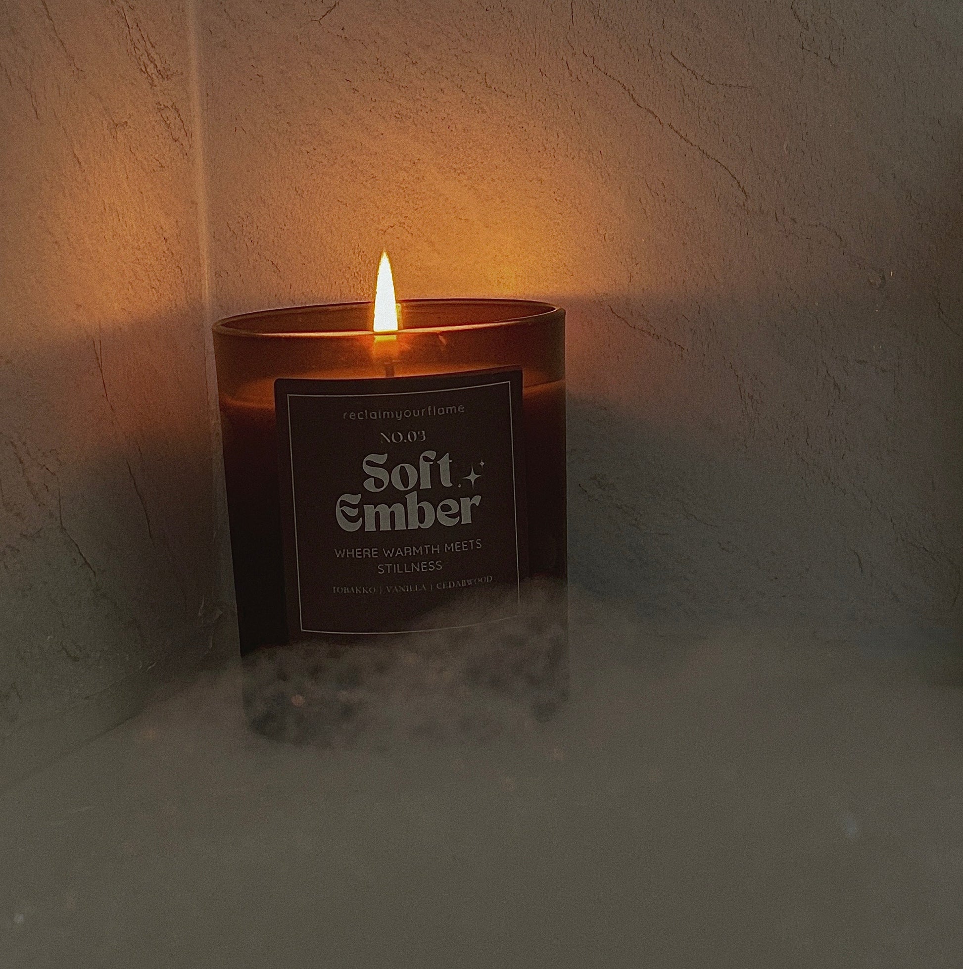 Candle labeled 'Soft Ember' in a textured wall corner