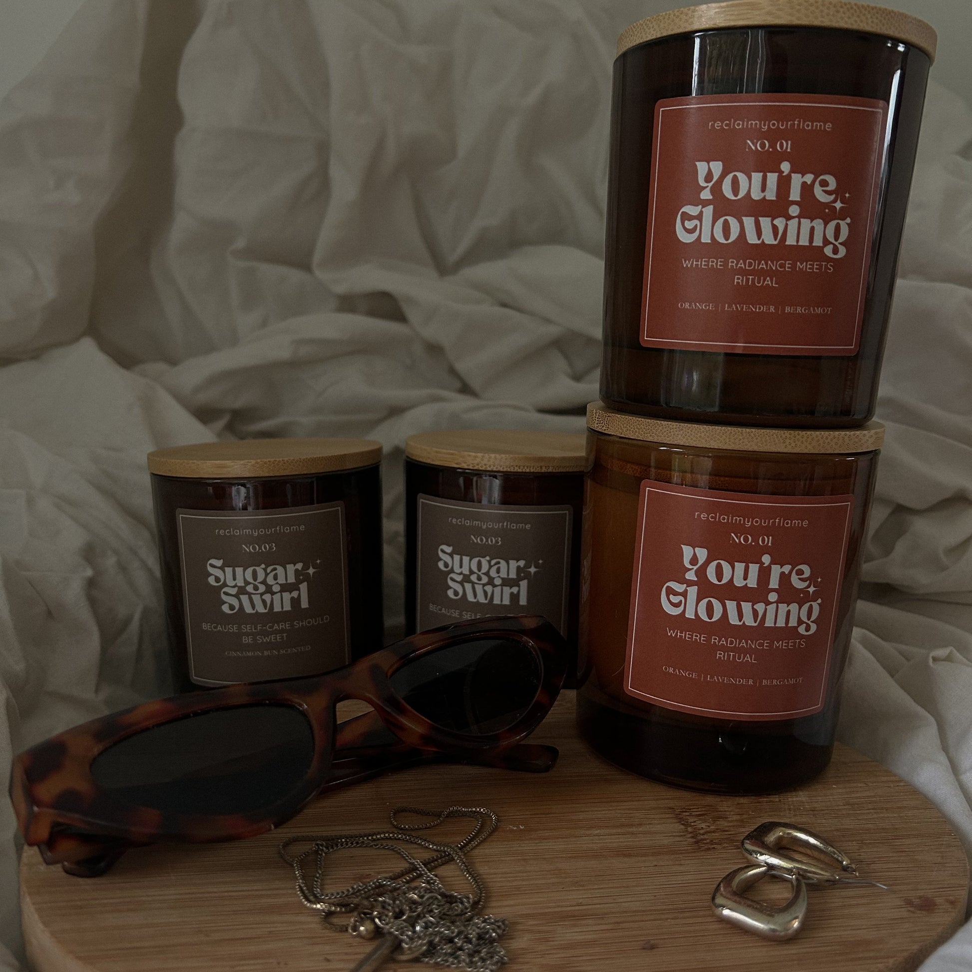Four candles labelled 'Sugar Swirl' and 'You're Glowing' on a wooden tray with sunglasses and jewellery.
