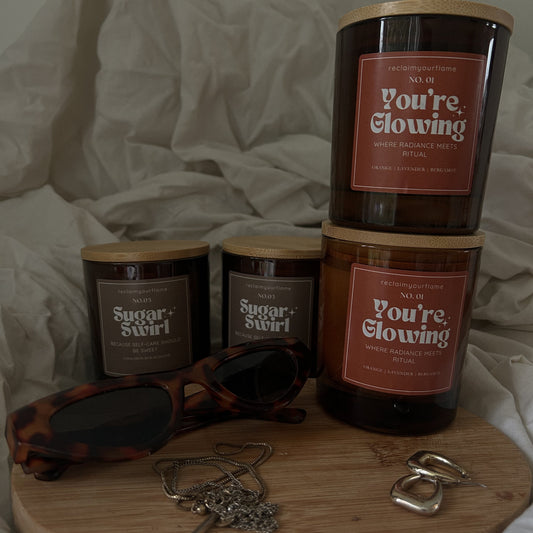 Four candles labelled 'Sugar Swirl' and 'You're Glowing' on a wooden tray with sunglasses and jewellery.
