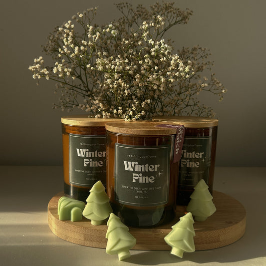 Three candles labeled 'Winter Pine' on a wooden stand with decorative elements.